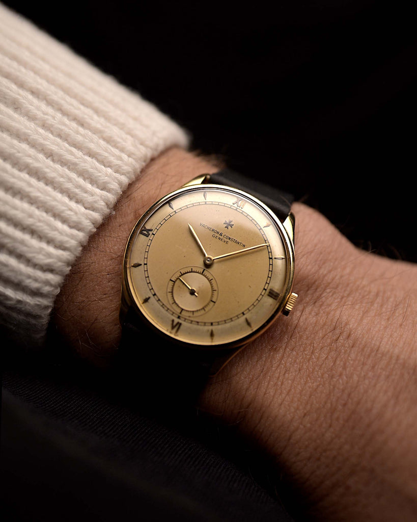 Vintage Vacheron Constantin Spillman Railroad watch from the 1940s on a wrist on black background. 35mm wide with 18k Yellow Gold Case, Manual Wind Movement, Champagne Dial with Patina and Black Leather Strap.