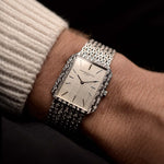 Vintage Vacheron Constantin 7457 Rectangular watch from the 1970s on a wrist on black background. 25mm wide, 18k White Gold, Manual wind Caliber 1003, Flawless silver linen dial and Braided bracelet.