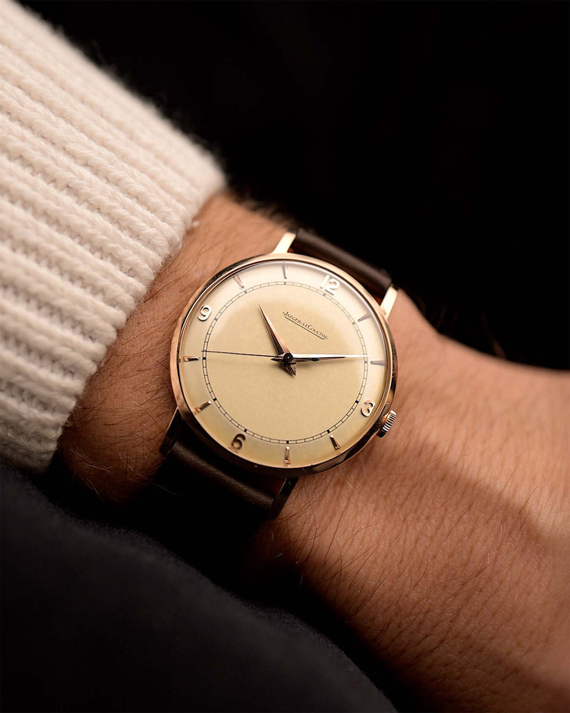 Rosegold Vintage Jaeger LeCoultre 18k Rose Railroad watch from the 1950s on a person's wrist with a dark background. 35mm wide with 18k Rose Gold Case, Manual Wind Caliber P450/4C, Cream Dial and Brown Leather Strap.