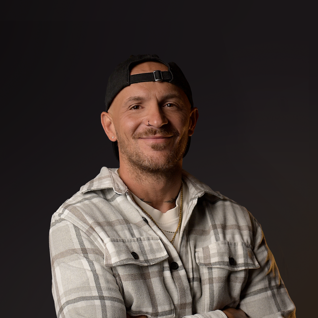 Man wearing a plaid shirt and cap against a dark background