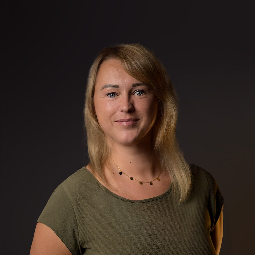 Woman with blonde hair wearing a green top against a dark background