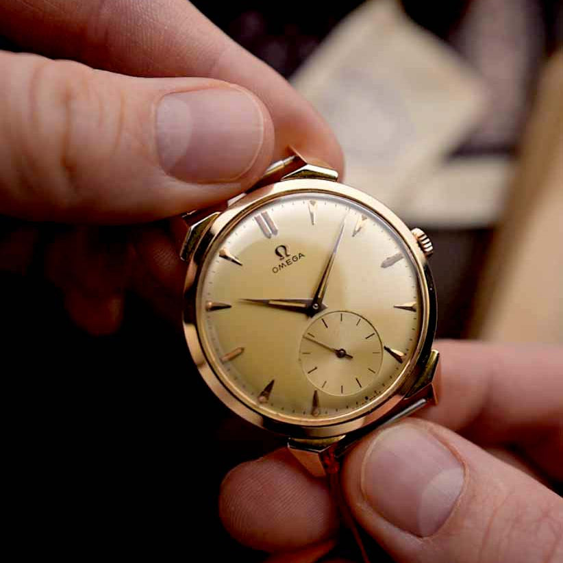 Goldene Vintage-Omega-Uhr, die sanft mit beiden Händen gehalten wird.