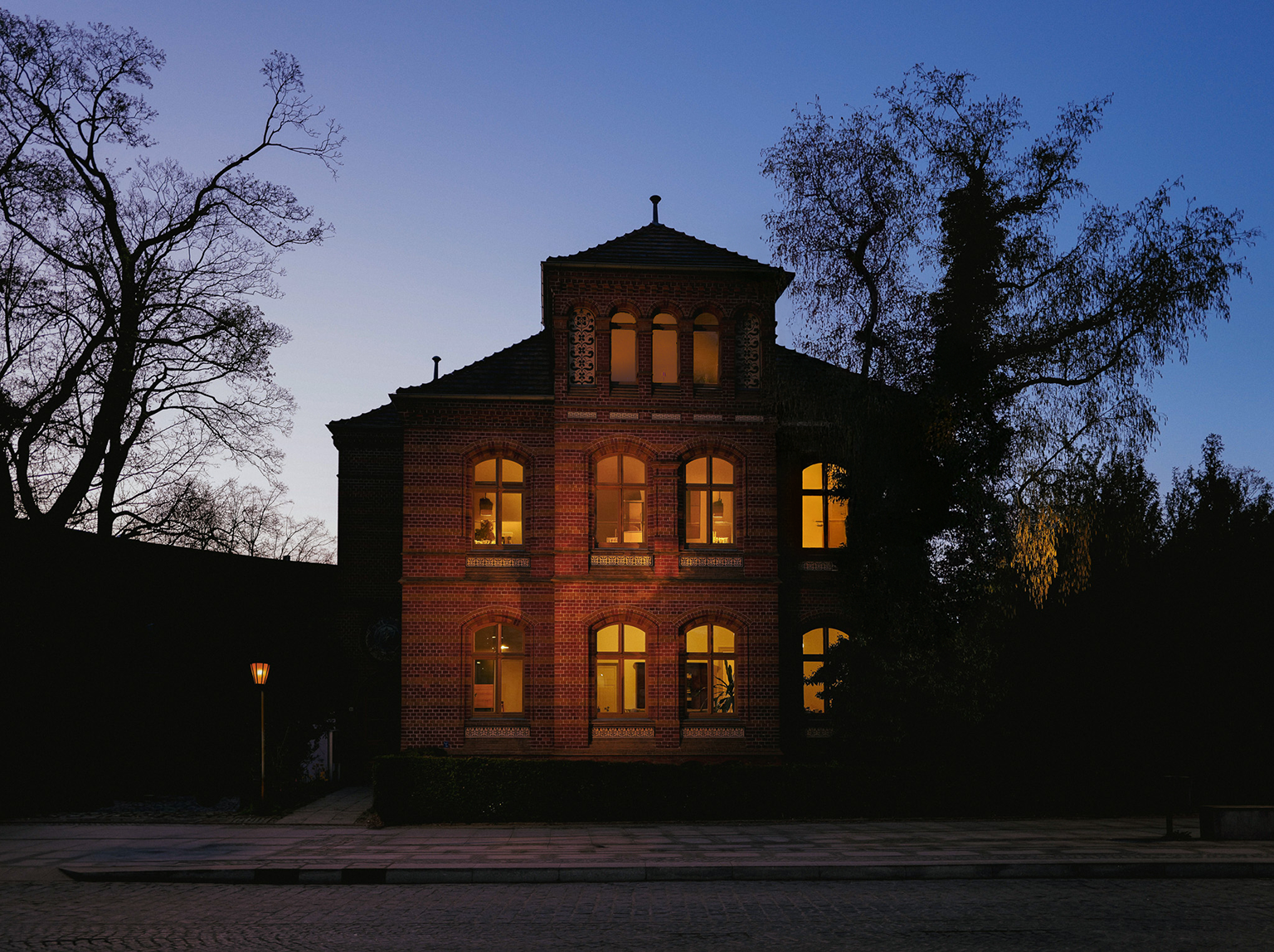 Dunkles Gebäude mit beleuchteten Fenstern bei Nacht, umgeben von Bäumen