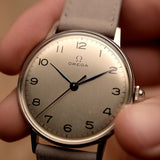 Vintage Omega 2325 Jumbo Leaf Uhr, silbernes Zifferblatt, Edelstahlgehäuse, graues Lederband, in der Hand gehalten vor einem unscharfen Hintergrund