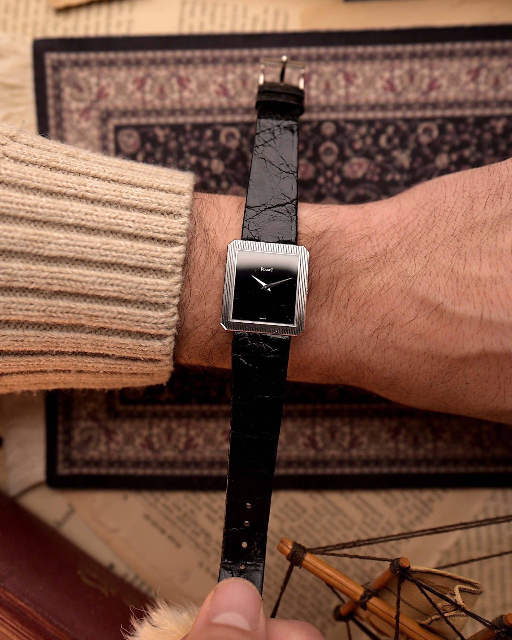 Vintage Piaget Protocole 9154 Uhr, aus 18 Karat Weißgold, mit Onyx-Zifferblatt, Tank-Gehäuse, 9P Handaufzug, Lederarmband am Handgelenk, auf einer gemusterten Oberfläche.