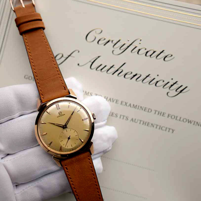 Vintage-Omega-Uhr, die von einer behandschuhten Hand über ein Echtheitszertifikat gehalten wird.