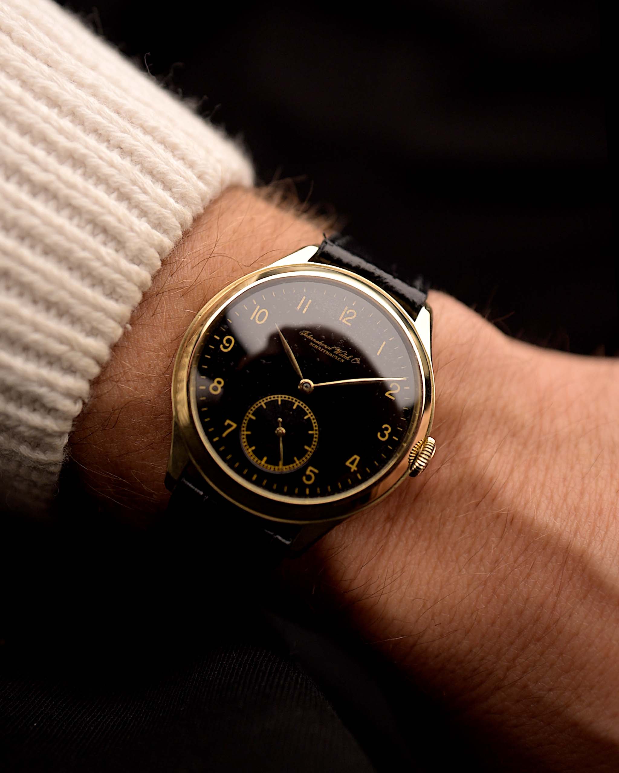 Vintage IWC Pre Hermet Uhr, aus 14 Karat Gelbgold, schwarz vergoldetes Zifferblatt, Cal 83 Handaufzug, schwarzes Lederarmband an einem Handgelenk vor schwarzem Hintergrund, Video