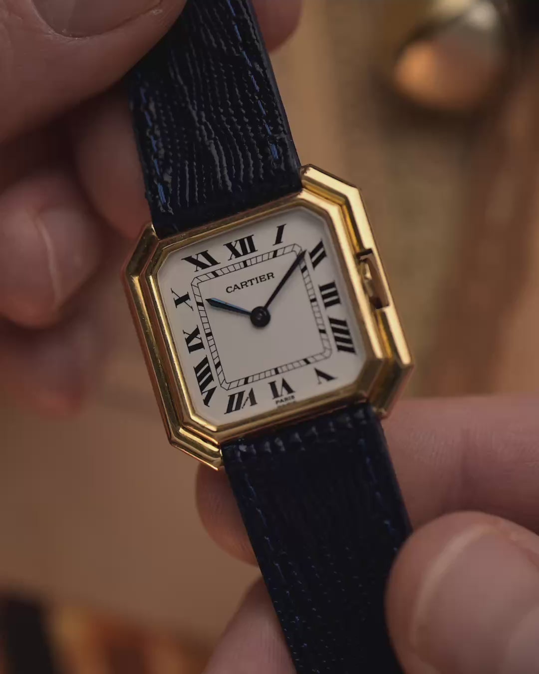 Vintage Cartier Ceinture 78099 Uhr mit quadratischem Gehäuse aus 18 Karat Gelbgold, weißem Zifferblatt, Handaufzug und blauem Lederarmband auf unscharfem Hintergrund, Video mit Details