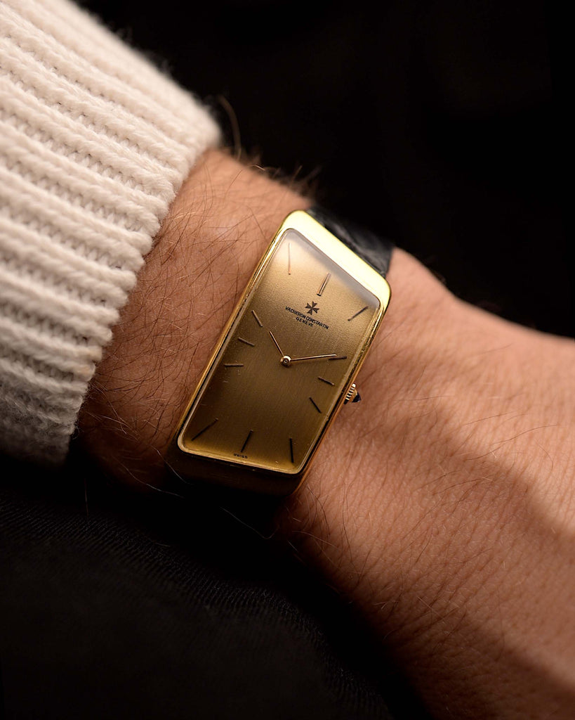 Vacheron Constantin 35202 Prestige de la France from the 1970s on a wrist on black background. 32mm wide with 18k Yellow Gold trapezium-shaped Case, Manual Caliber 1150/B, Flawless Golden Dial and Original Black Leather Strap.