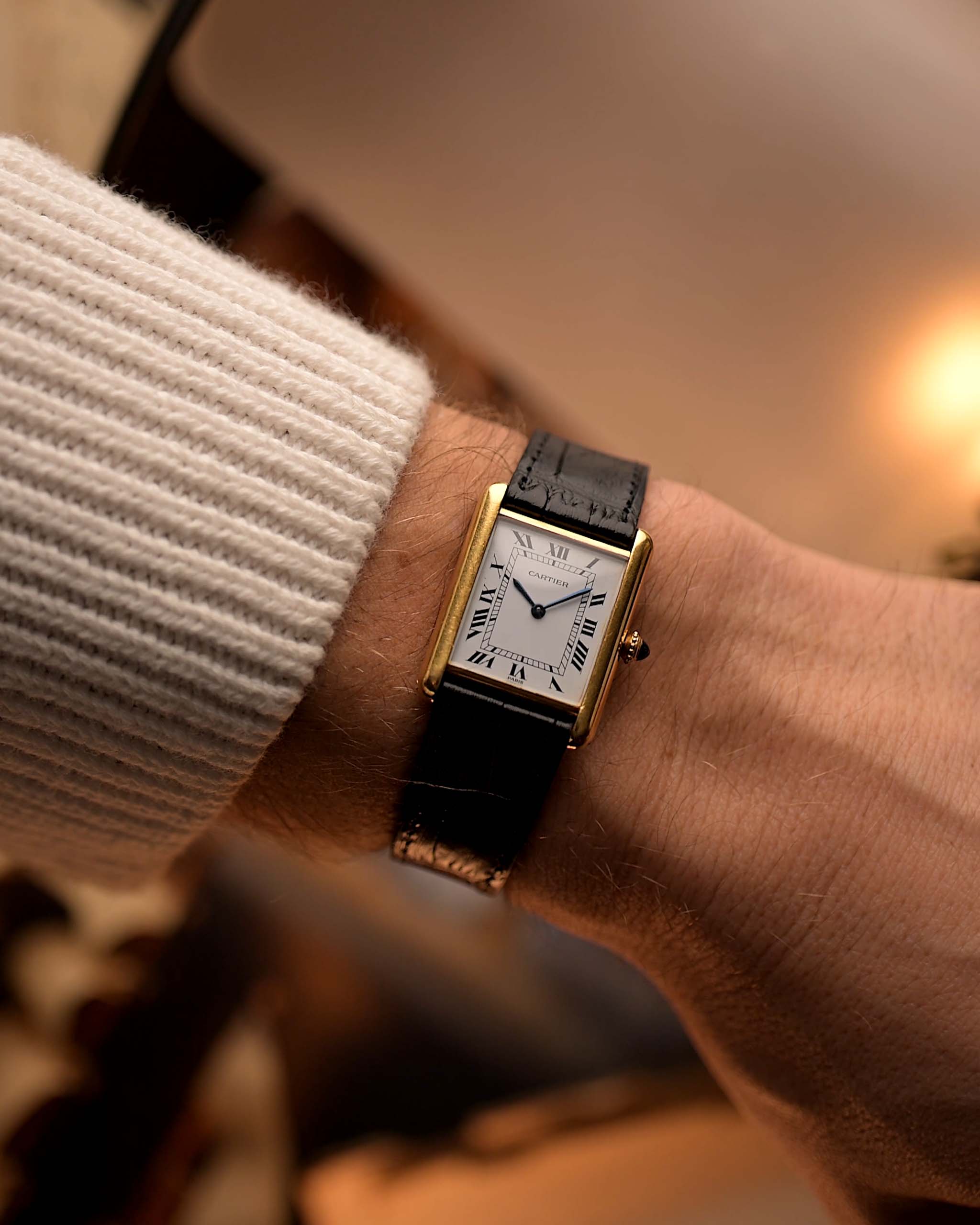 Reloj Cartier Tank Louis vintage, oro amarillo de 18 quilates, esfera blanca, movimiento manual, con correa de aligátor negra, en una muñeca, fondo borroso