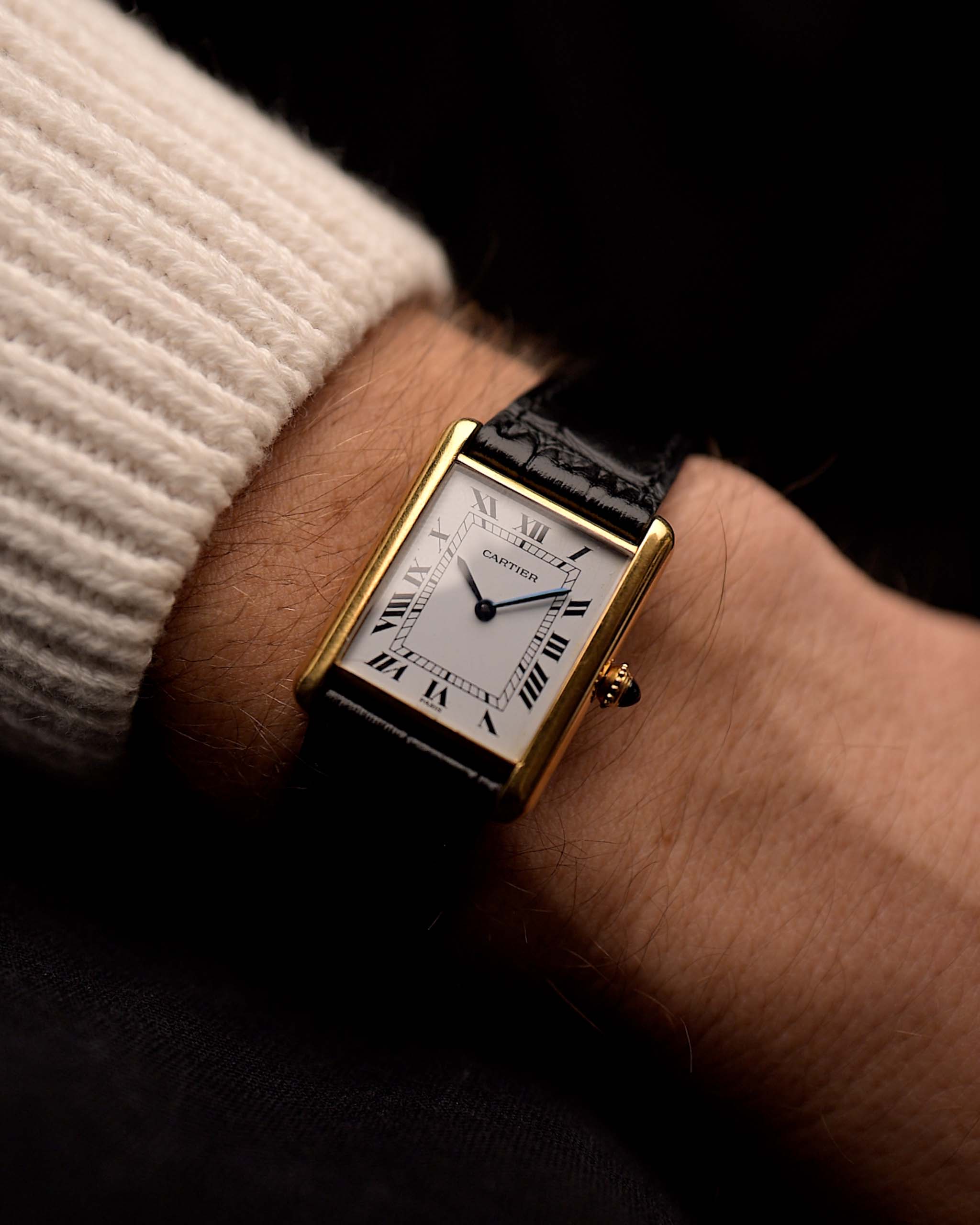 Reloj Cartier Tank Louis vintage, oro amarillo de 18 quilates, esfera blanca, movimiento manual, con correa de aligátor negra, en una muñeca, fondo negro