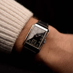 Reloj vintage Omega de jeringuilla rectangular, esfera dorada negra, caja de acero inoxidable, movimiento manual, con correa de cuero negro, en una muñeca sobre fondo negro