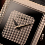 Primer plano de un reloj Piaget Protocole 9151 Vintage, oro blanco de 18 quilates, esfera de ónice, forma de tanque, movimiento Calibre 9P, correa de piel, en una muñeca, fondo borroso