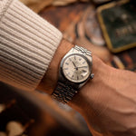 Reloj Rolex Datejust 1601 vintage, esfera plateada con efecto sol, caja de acero inoxidable, movimiento automático, brazalete Jubilee, en la muñeca, fondo borroso