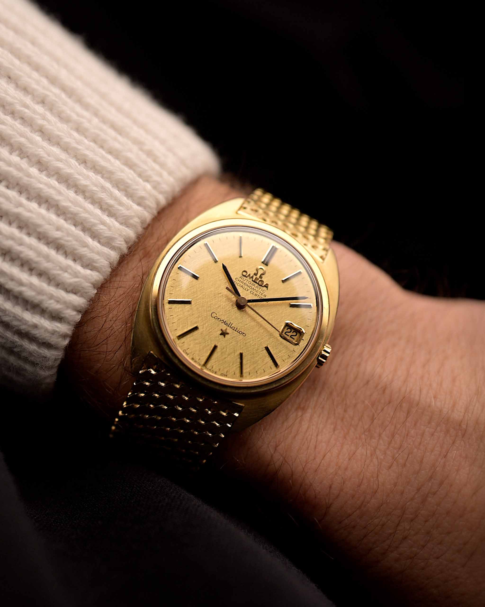 Reloj vintage Omega Constellation 168009 C-Shape 1966, oro amarillo de 14 quilates, esfera de lino, brazalete de oro en la muñeca de una persona con fondo oscuro, vídeo
