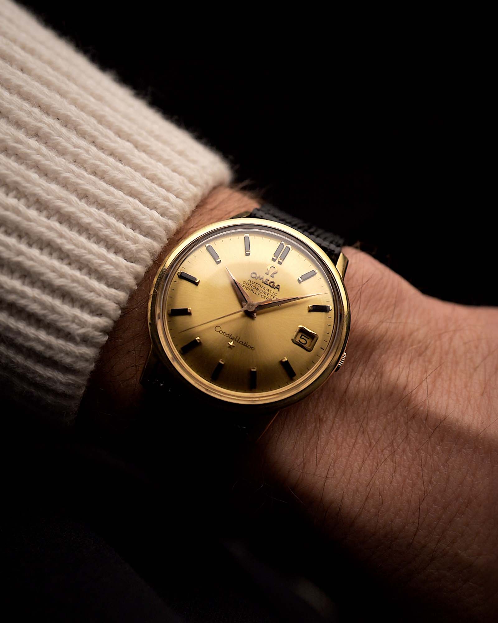 Reloj Omega Constellation 168010 vintage, oro amarillo de 18 quilates, esfera dorada con efecto rayos de sol, movimiento automático, en una muñeca sobre fondo negro, vídeo.