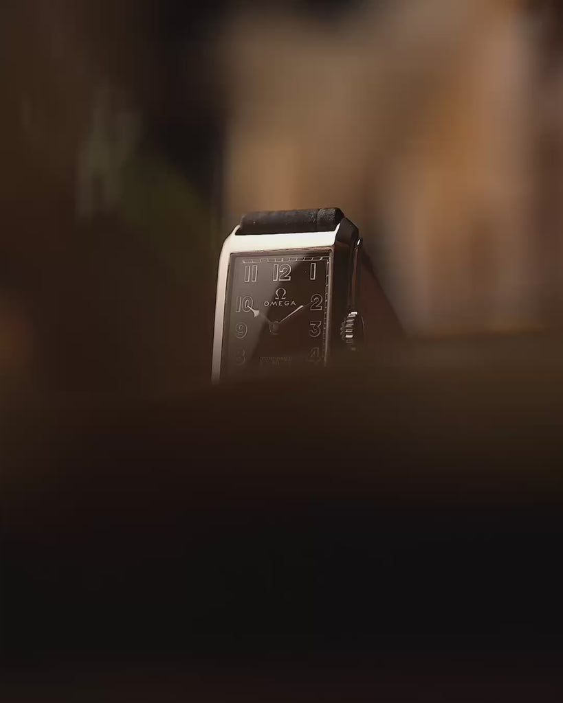 Reloj vintage Omega de jeringuilla rectangular, esfera dorada negra, caja de acero inoxidable, movimiento manual, con correa de cuero negro, fondo borroso, vídeo