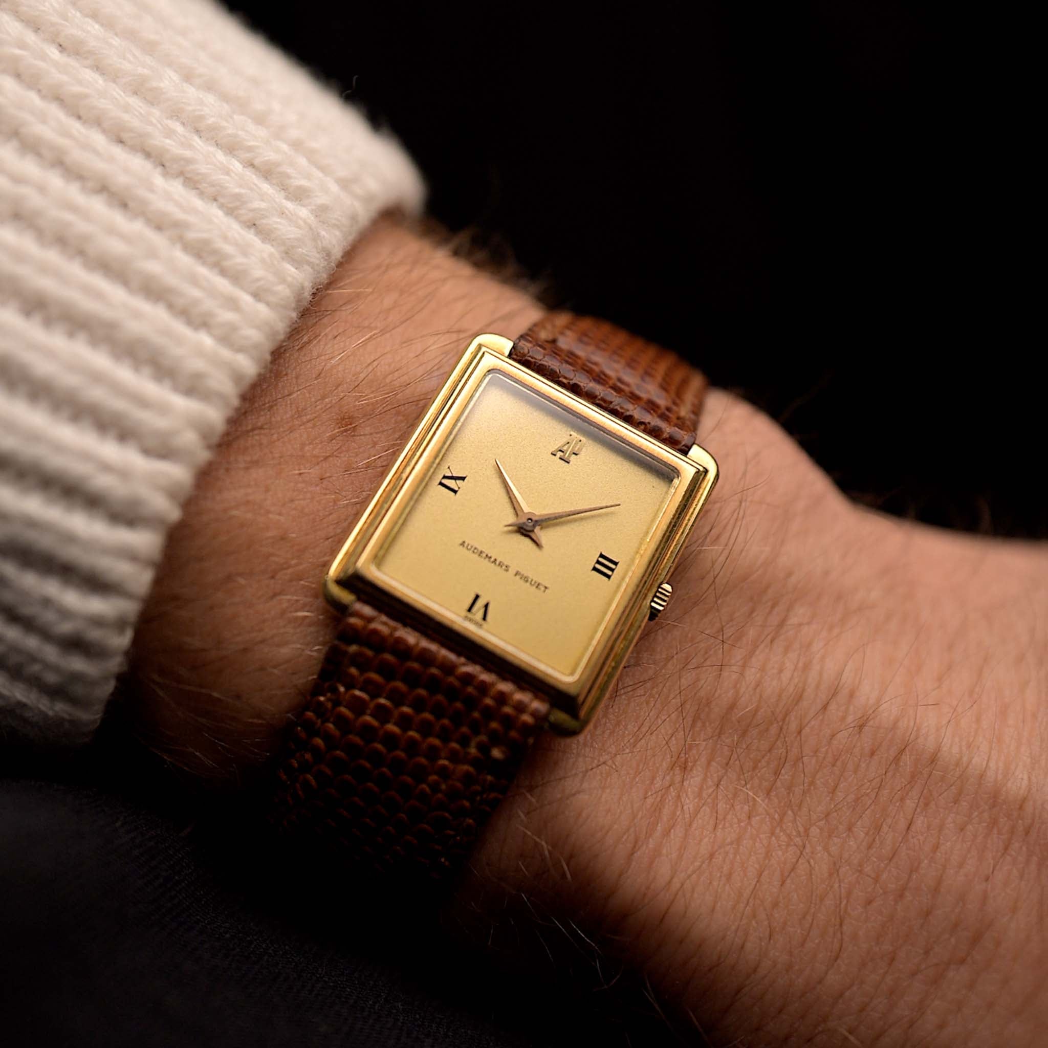 Vintage Audemars Piguet Square watch, 18k gold, golden satin dial, leather strap, on wrist, black background