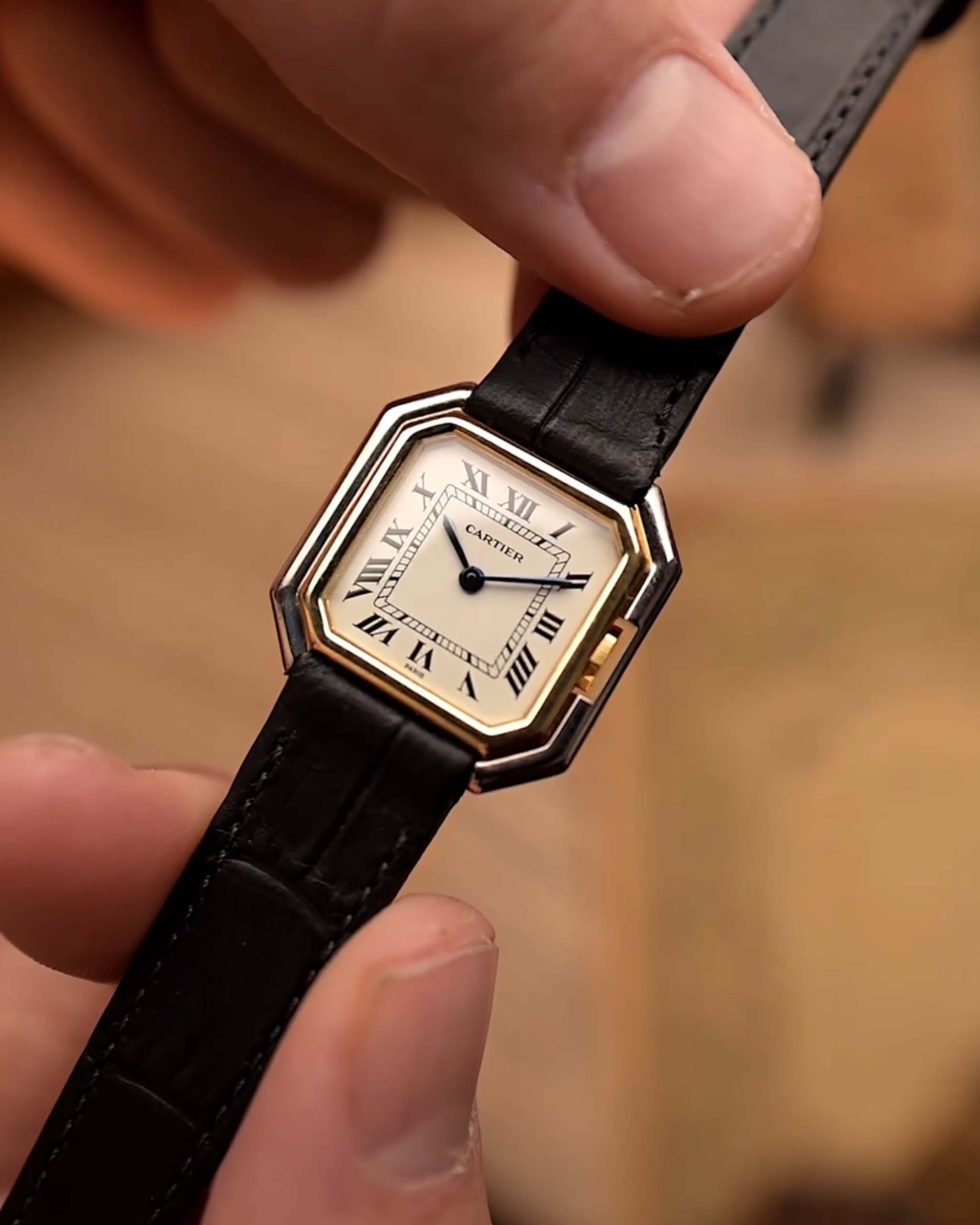 Montre vintage Cartier Ceinture des années 1980, or bicolore, cadran blanc, boîtier carré, tenue par une main sur un fond flou.