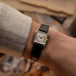 Montre vintage Cartier Ceinture des années 1980, or bicolore, cadran blanc, boîtier carré, sur un poignet sur fond flou