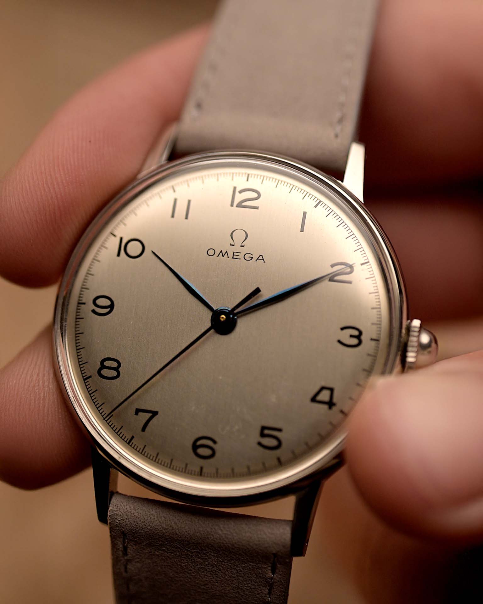 Montre Omega 2325 Jumbo Leaf vintage, cadran argenté, boîtier en acier inoxydable, bracelet en cuir gris, tenue à la main sur fond flou