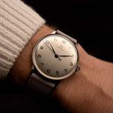 Montre Omega 2325 Jumbo Leaf vintage, cadran argenté, boîtier en acier inoxydable, mouvement à remontage manuel, bracelet en cuir gris, au poignet, fond noir