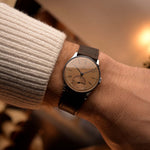 Montre vintage Omega Art Deco avec cadran saumon, boîtier en acier inoxydable, mouvement à remontage manuel et bracelet en cuir marron au poignet sur fond flou