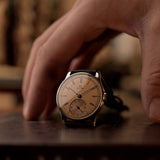 Montre Vintage Omega Art Deco avec cadran saumon, boîtier en acier inoxydable et bracelet en cuir marron sur une surface en bois avec une aiguille et un arrière-plan flous.