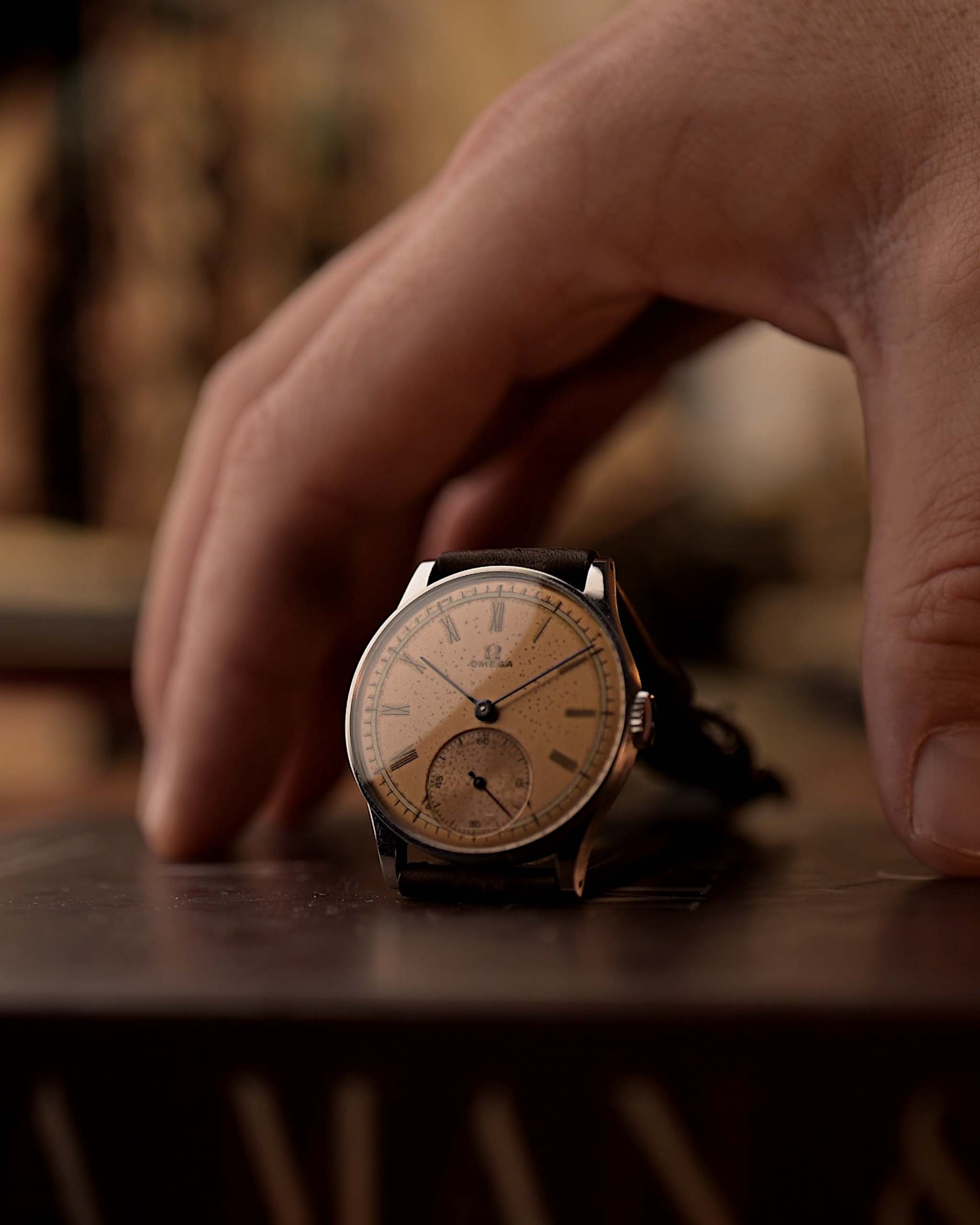 Montre Vintage Omega Art Deco avec cadran saumon, boîtier en acier inoxydable et bracelet en cuir marron sur une surface en bois avec une aiguille et un arrière-plan flous.