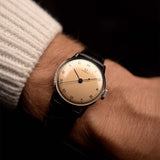 Montre Omega Medicus Salmon Roman de 1944 au poignet. 28 mm, acier inoxydable, calibre 23.4 SC à remontage manuel, cadran saumon impeccable, chiffres romains et bracelet en cuir noir.
