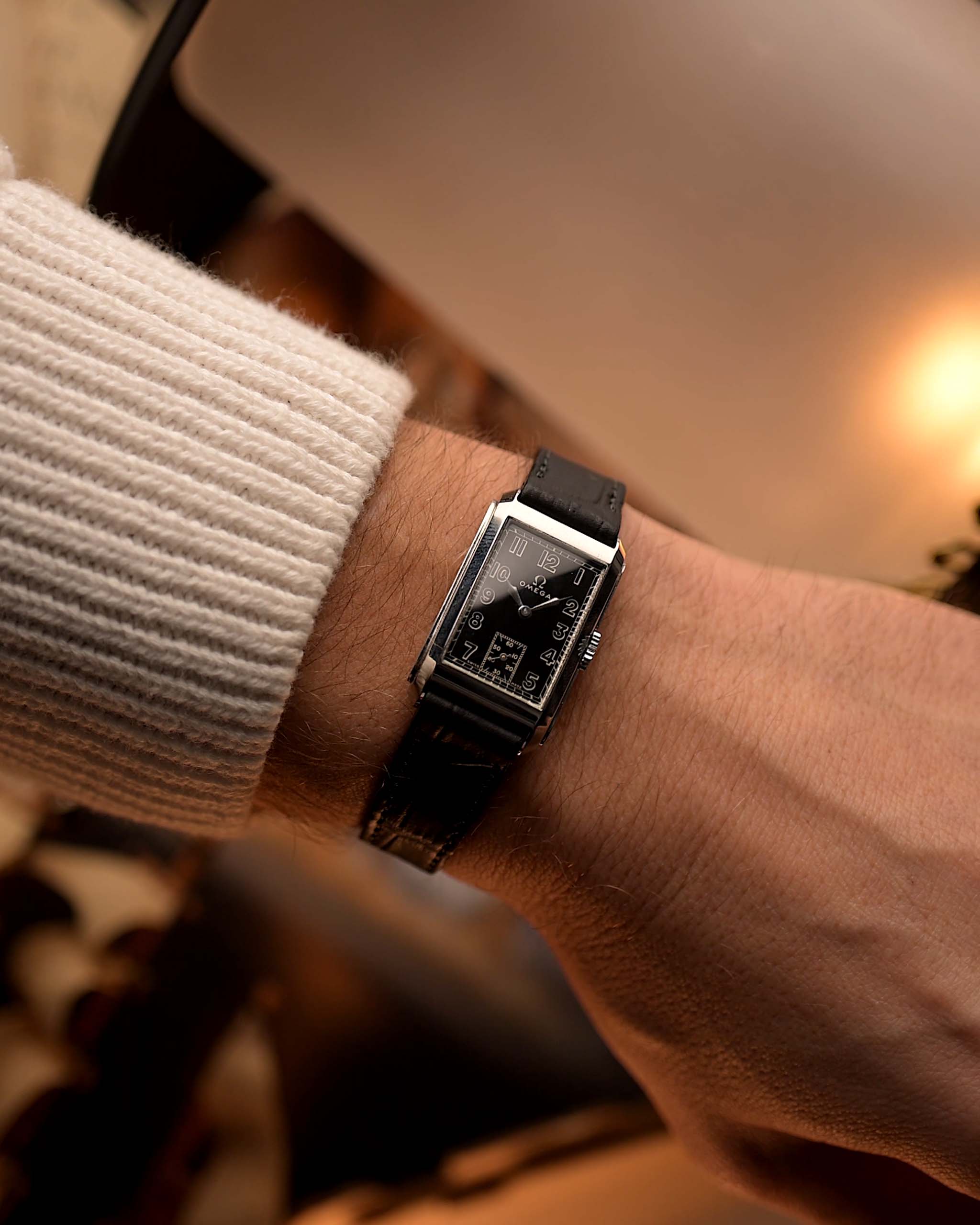 Montre Omega Rectangular Syringe vintage, cadran noir doré, boîtier en acier inoxydable, mouvement manuel, sur bracelet en cuir noir, au poignet sur fond flou