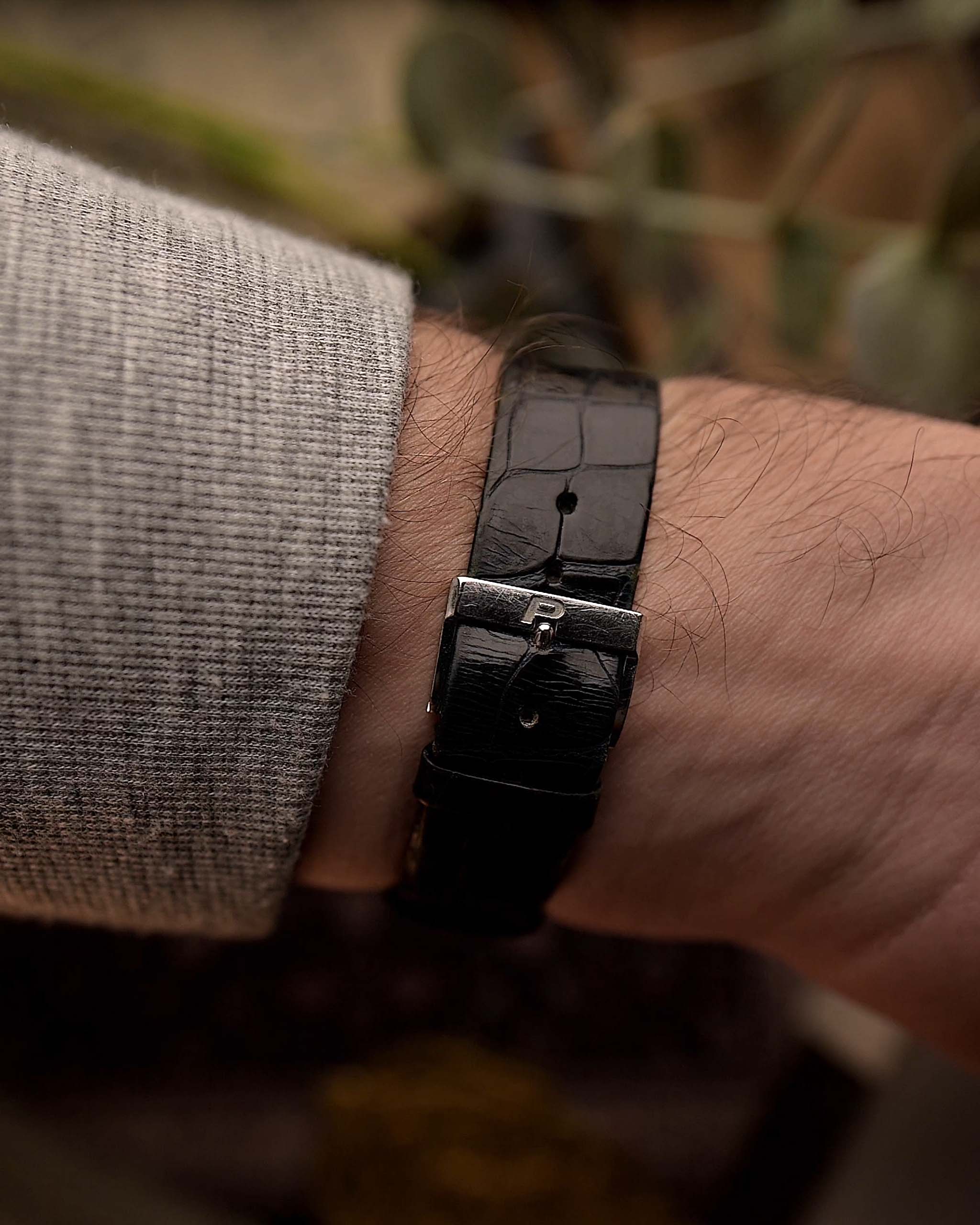 Gros plan d'une montre Piaget Protocole 9151 vintage, bracelet cuir, or blanc 18 carats, cadran Onyx, forme tank, mouvement Calibre 9P, bracelet cuir, sur un poignet, fond flou