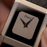 Gros plan du cadran d'une montre Piaget Protocole 9151 vintage, or blanc 18 carats, cadran en onyx, forme tank, mouvement Calibre 9P, bracelet en cuir, sur un poignet, fond flou