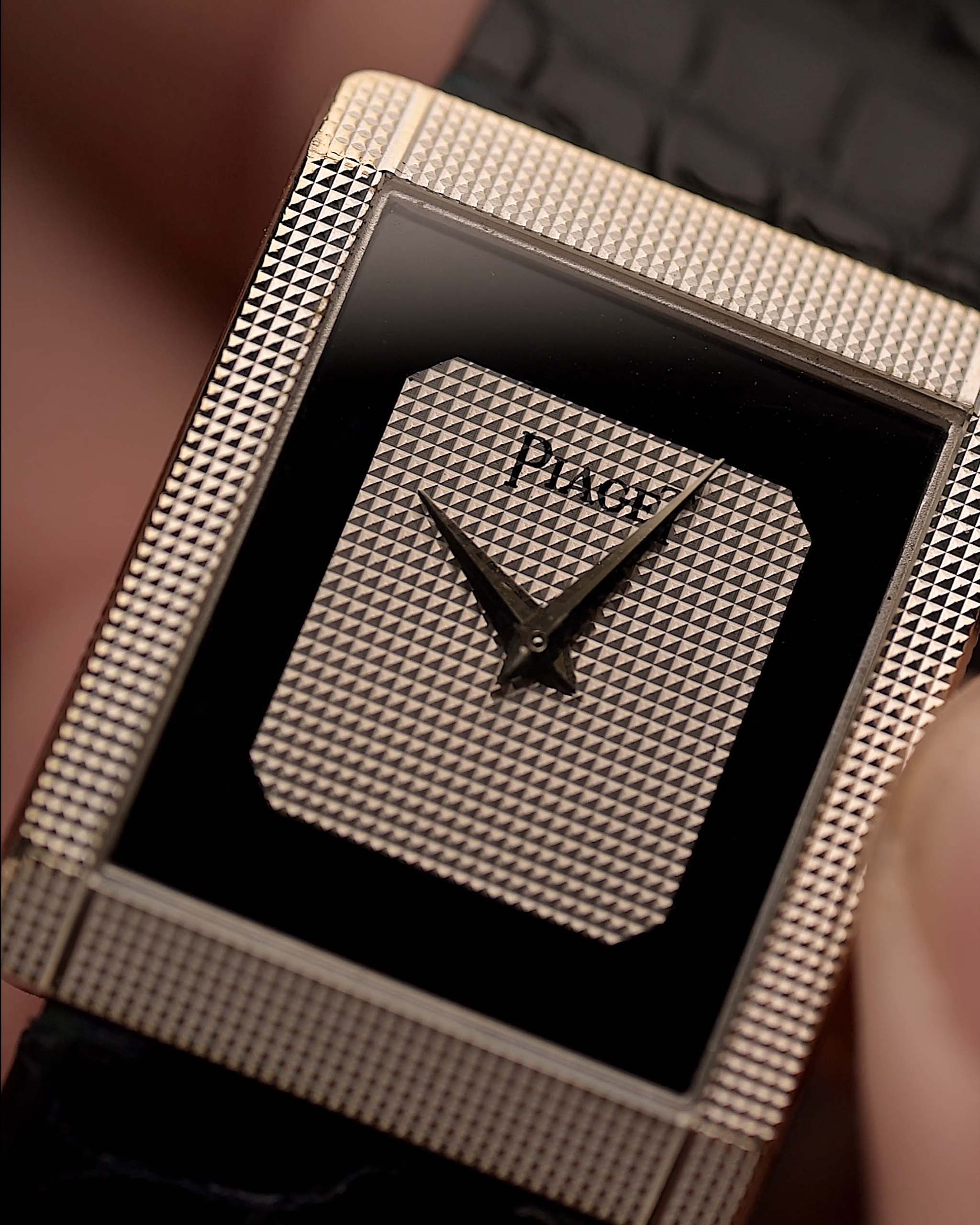 Gros plan du cadran d'une montre Piaget Protocole 9151 vintage, or blanc 18 carats, cadran en onyx, forme tank, mouvement Calibre 9P, bracelet en cuir, sur un poignet, fond flou