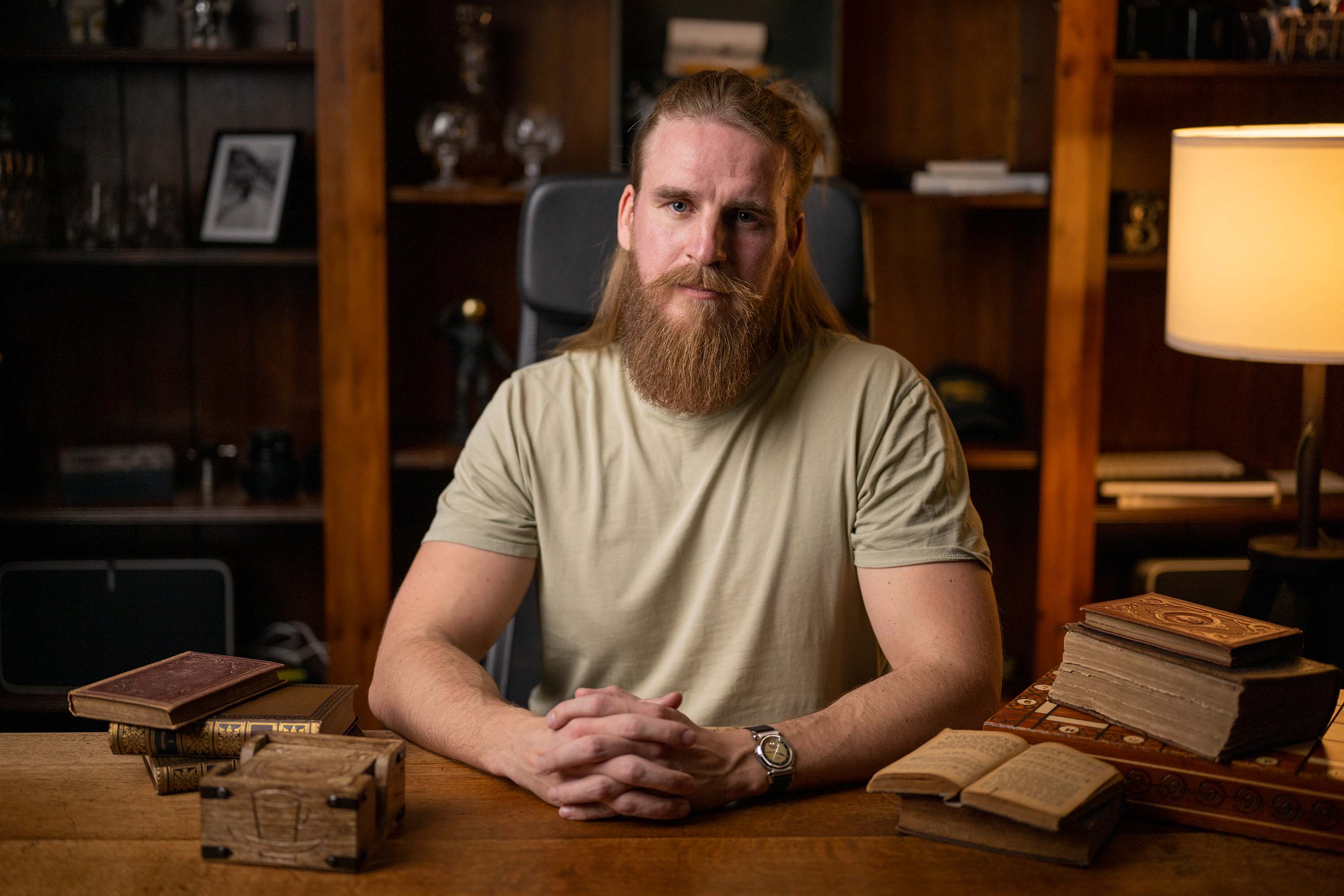 Homme avec une longue barbe portant un T-shirt beige, assis à une table.