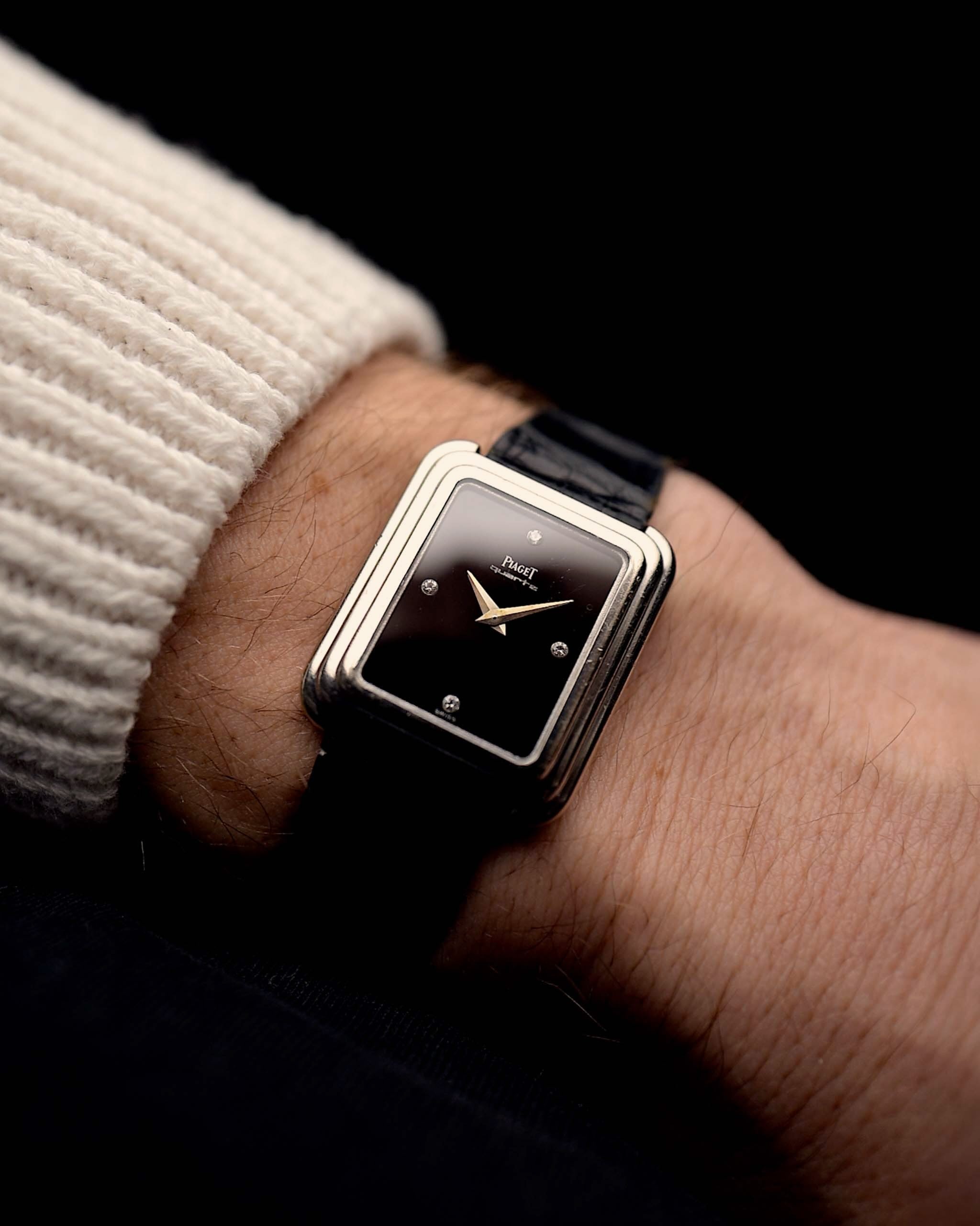 Piaget Protocole 74101 Montre Vintage des années 1980 au poignet sur fond noir. Largeur 26 mm, boîtier en or blanc 18 carats, cadran en onyx avec 4 diamants, mouvement à quartz et bracelet en cuir noir d'origine.