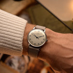 Orologio vintage Omega 2325 Jumbo Leaf, quadrante argento, cassa in acciaio inossidabile, movimento a carica manuale, cinturino in pelle grigio, al polso, sfondo sfocato