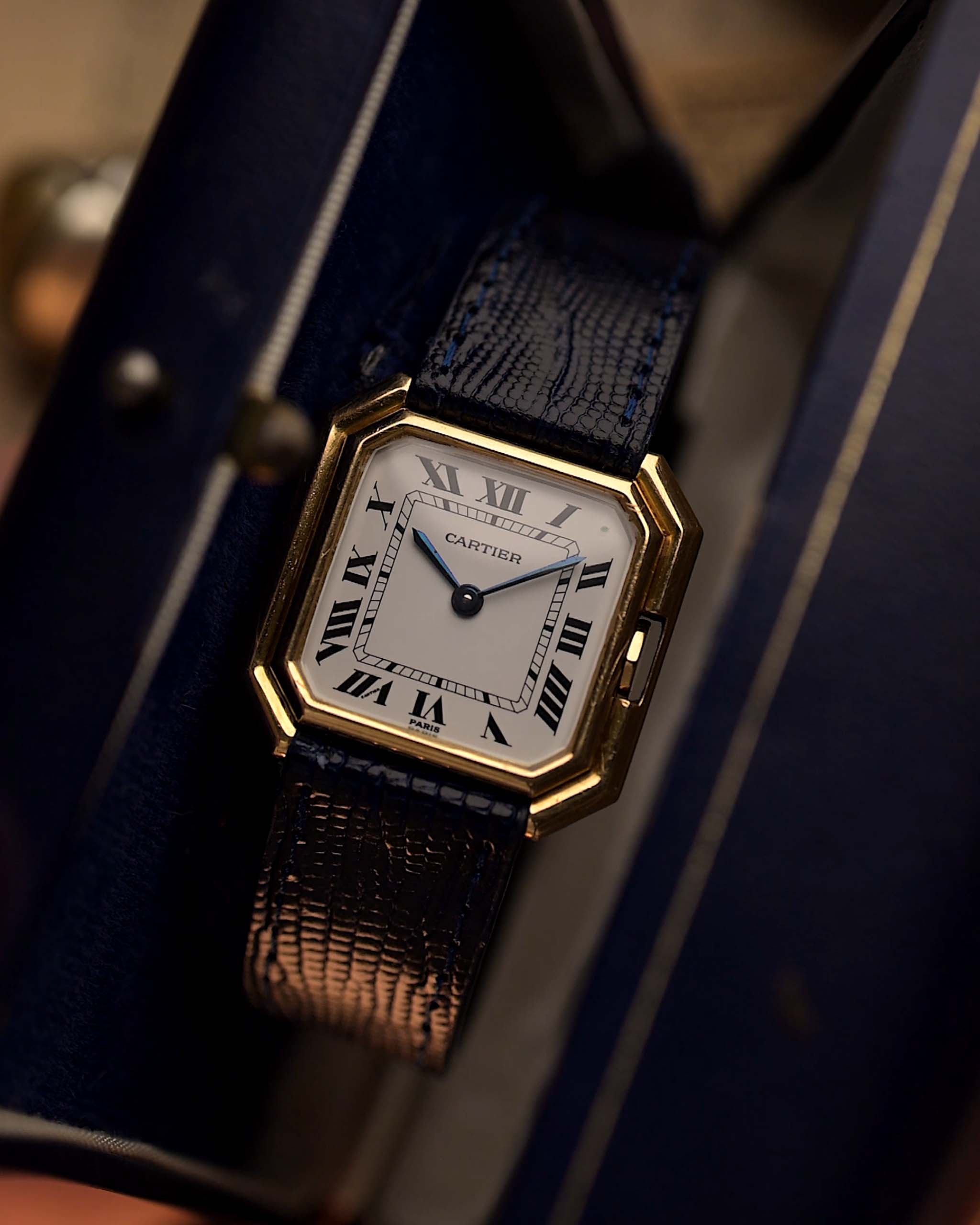 Orologio vintage Cartier Ceinture 78099 con cassa quadrata in oro giallo 18 carati, quadrante bianco, carica manuale, cinturino in pelle blu su sfondo sfocato.