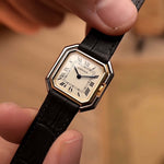 Orologio vintage Cartier Ceinture degli anni '80, oro bicolore, quadrante bianco, cassa quadrata, tenuto da una mano su uno sfondo sfocato.