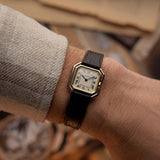 Orologio vintage Cartier Ceinture degli anni '80, oro bicolore, quadrante bianco, cassa quadrata, su un polso su sfondo sfocato.