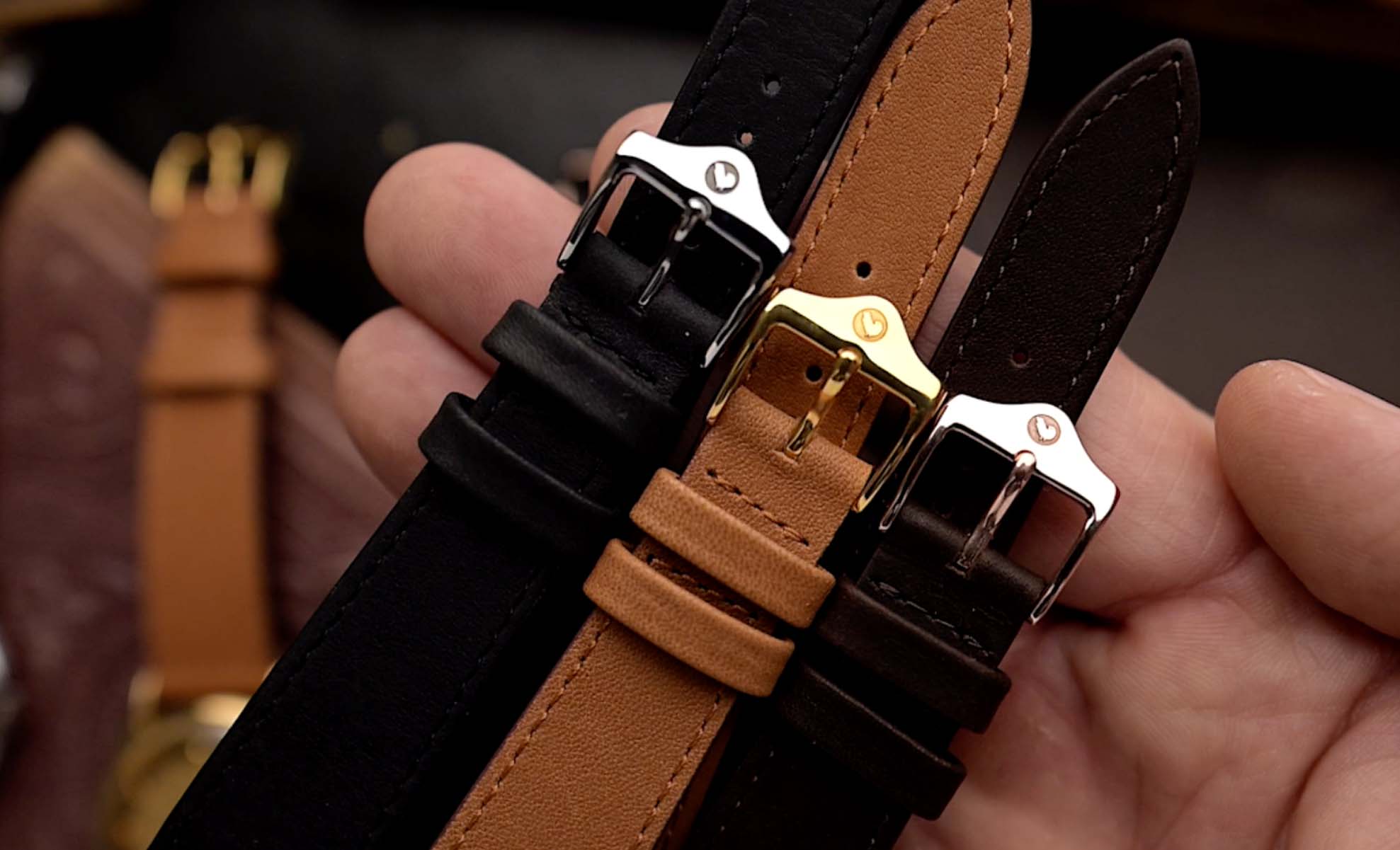 Cinturini in pelle nera, marrone e cognac con fibbie in metallo lucido.