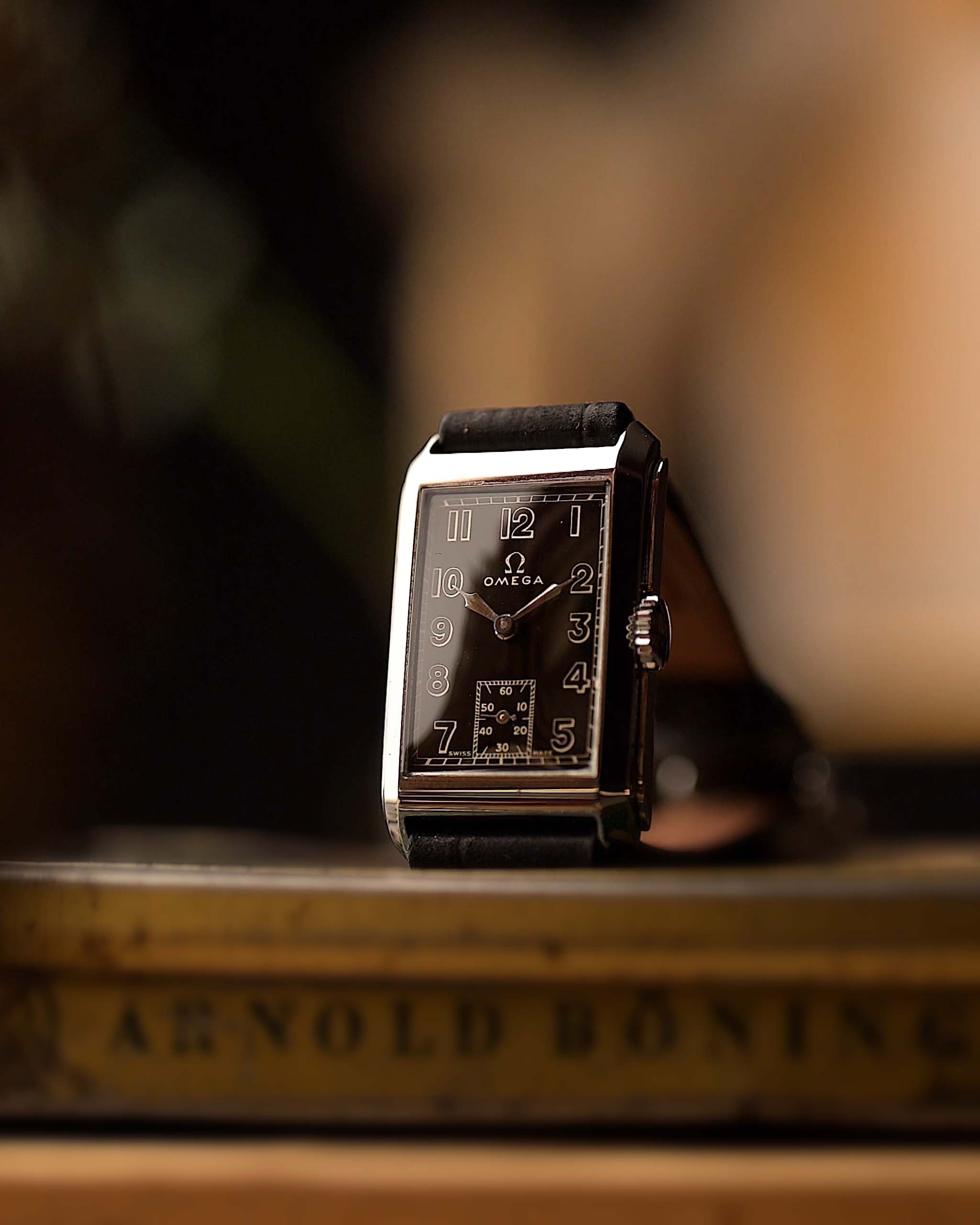 Orologio vintage Omega a siringa rettangolare, quadrante nero dorato, cassa in acciaio inossidabile, su una superficie di legno con sfondo sfocato