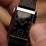 Orologio vintage Omega Siringa rettangolare, quadrante nero dorato, cassa in acciaio inossidabile, movimento manuale, su cinturino in pelle nera, tenuto in mano