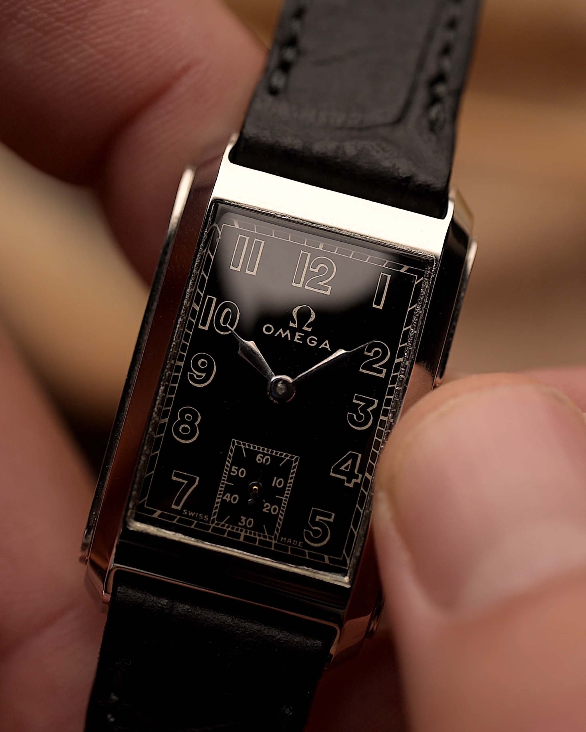 Orologio vintage Omega Siringa rettangolare, quadrante nero dorato, cassa in acciaio inossidabile, movimento manuale, su cinturino in pelle nera, tenuto in mano