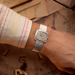 Orologio vintage Piaget TV 9574 con cassa TV in oro bianco 18 carati, quadrante in oro bianco, carica manuale, bracciale integrato su un polso con uno sfondo vintage.