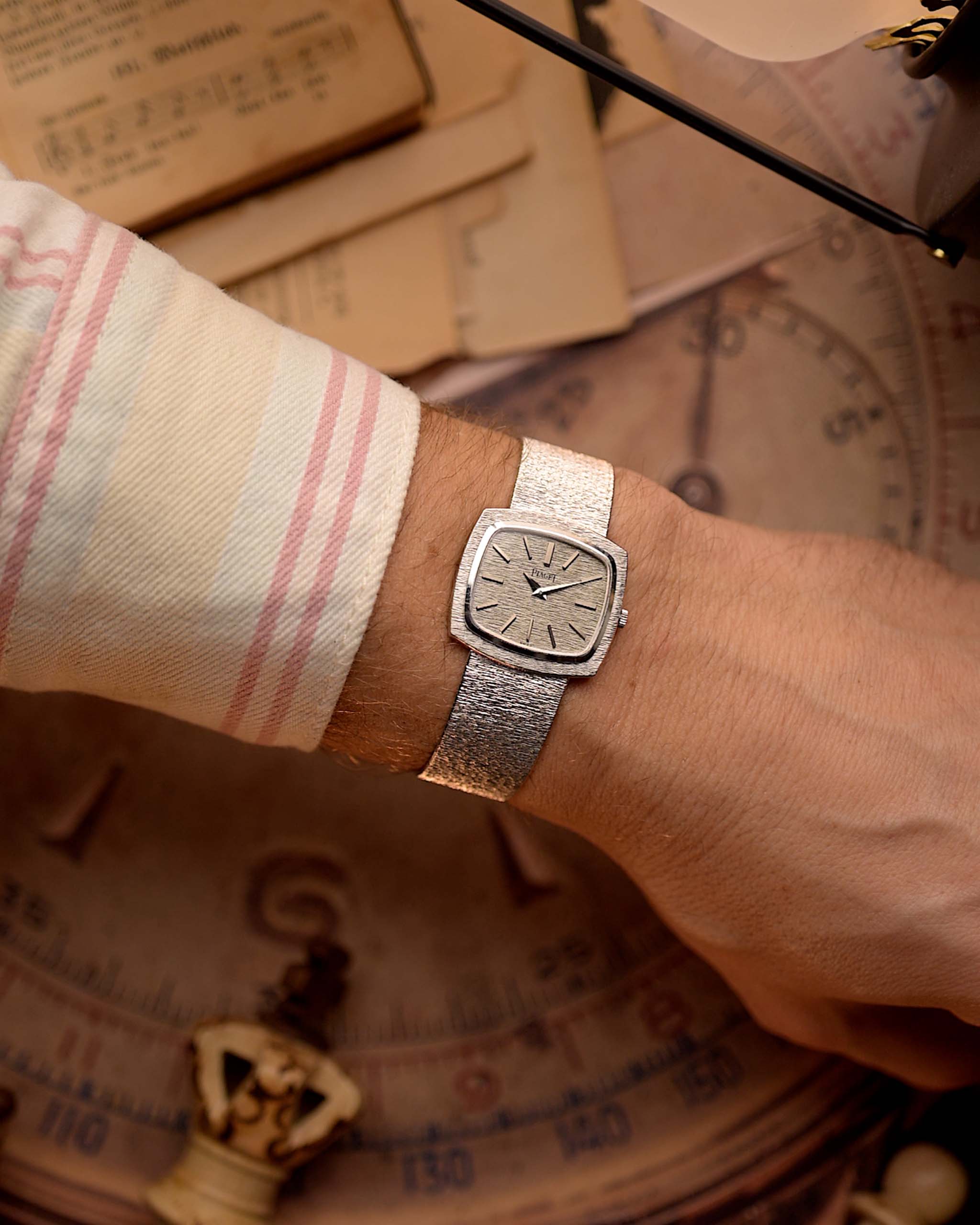 Orologio vintage Piaget TV 9574 con cassa TV in oro bianco 18 carati, quadrante in oro bianco, carica manuale, bracciale integrato su un polso con uno sfondo vintage.