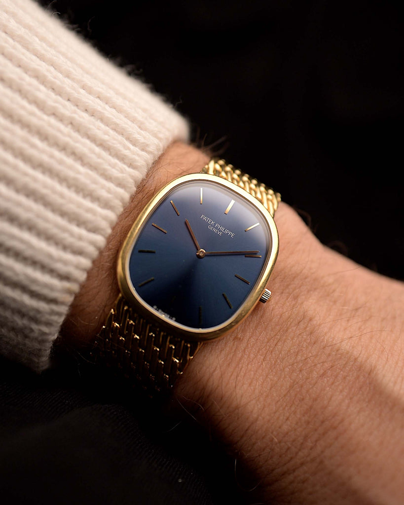 Patek Philippe 3738 Ellipse Jumbo Vintage Watch from the 1980s on a wrist on black background. 31mm wide with 18k Yellow Gold Case, Automatic Caliber 240, Flawless Blue Sunburst Sigma Dial and Yellow Gold Bracelet.