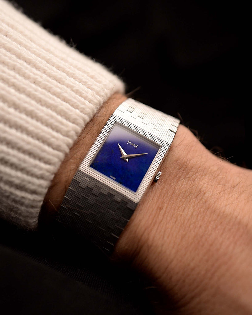 Piaget 9131 Lapislazuli 18k degli anni '70 al polso su sfondo nero. Largo 23 mm, in oro bianco 18 carati, con movimento a carica manuale, quadrante in Lapislazzuli blu impeccabile e bracciale integrato in oro bianco.