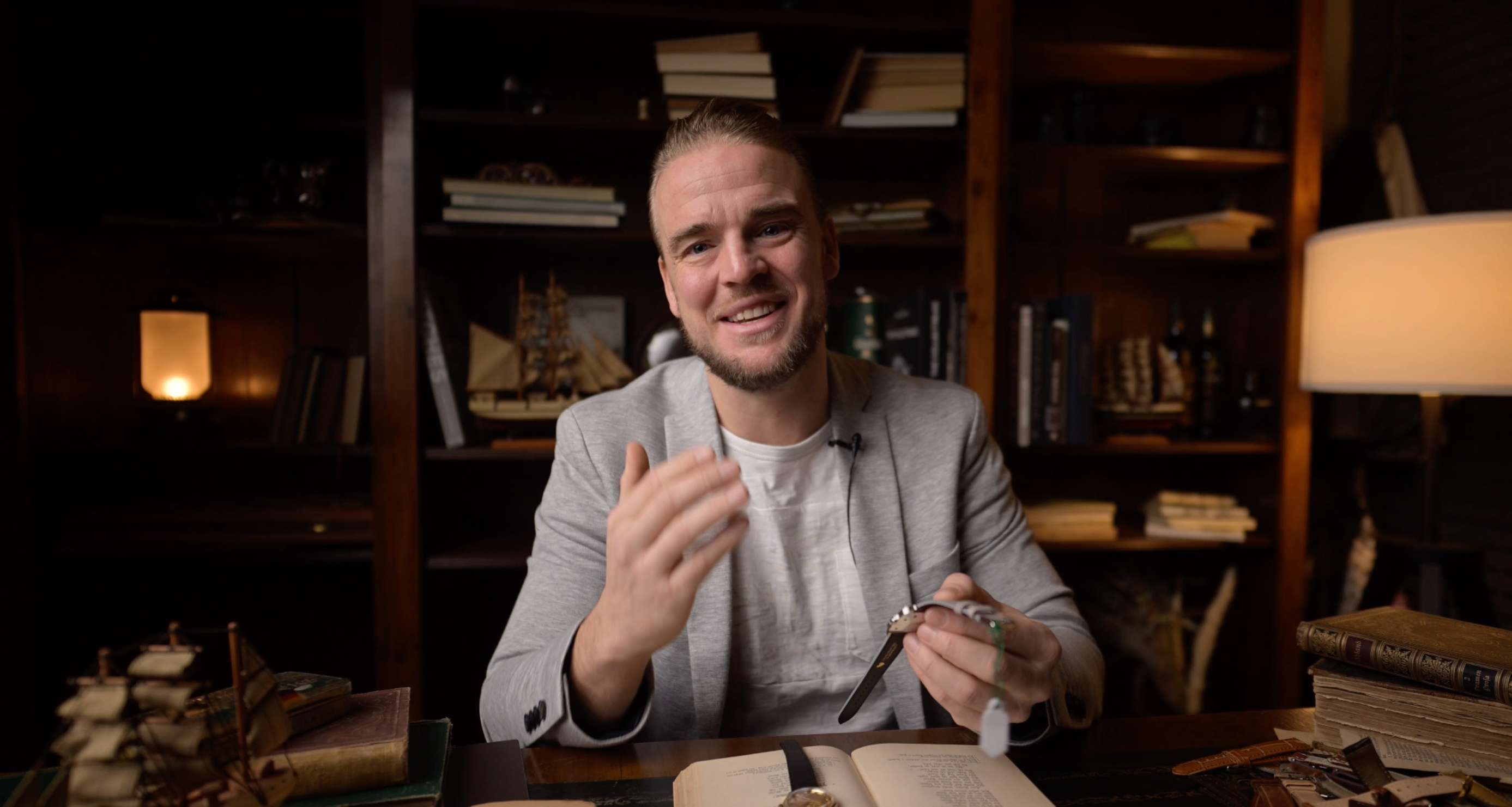 Uomo che presenta un orologio da polso alla scrivania di una biblioteca illuminata da luce calda.